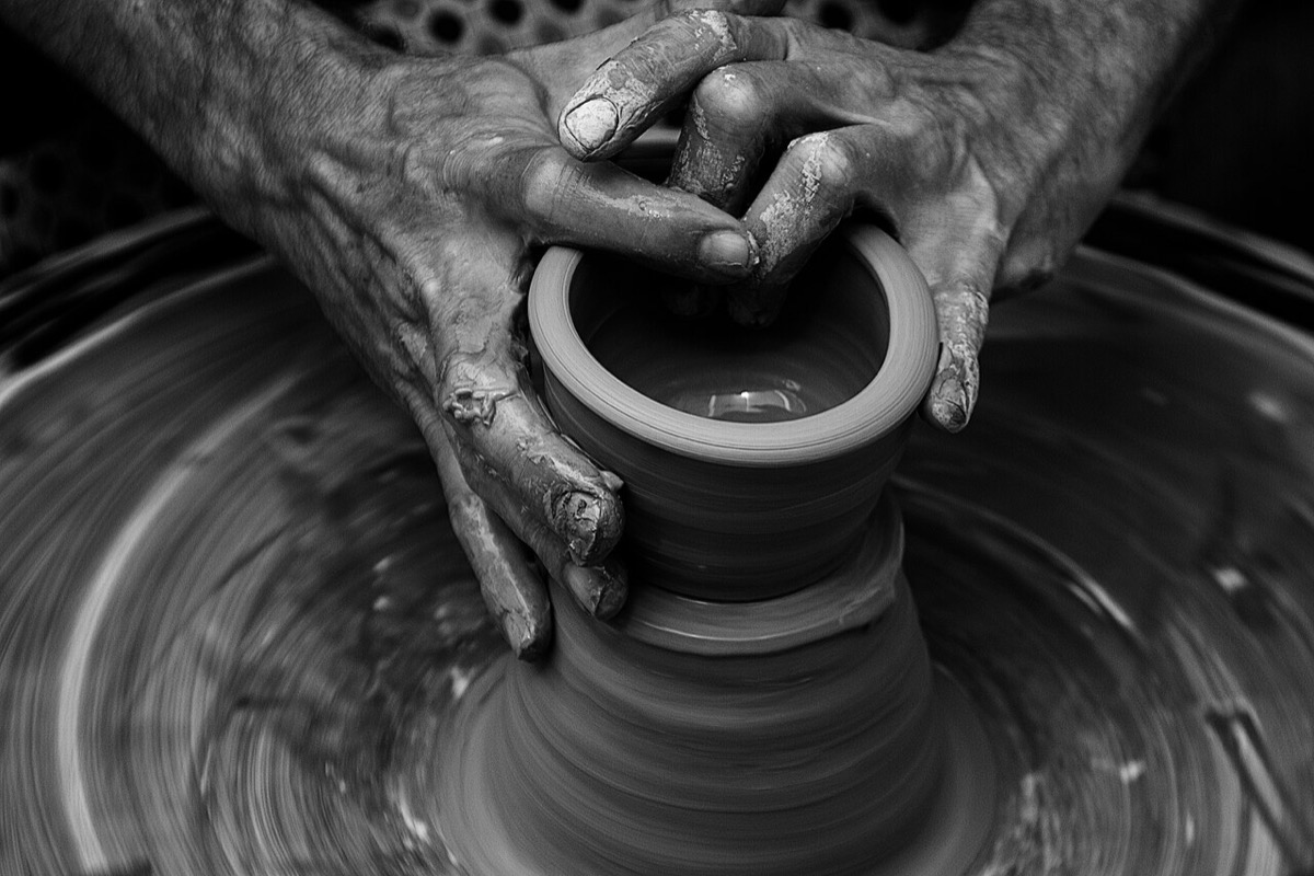 A potter's hands shaping a vessel on the wheel